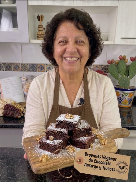 Doña Lupita sonriendo en su cocina, con la tabla de brownies veganos de chocolate y nueces en las manos